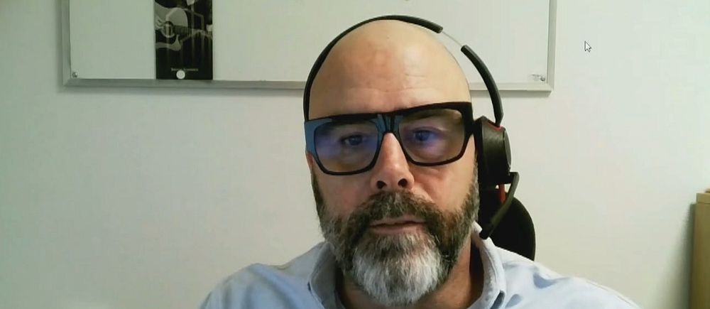 En man sitter på ett kontor med ett headset på huvudet och med en anslagstavla i bakgrunden