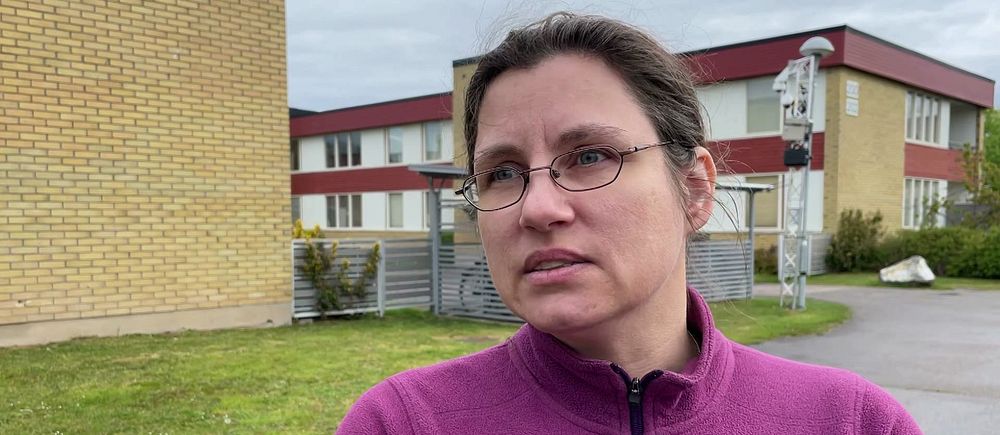 Person i lila tröja intervjuas utomhus framför en byggnad.