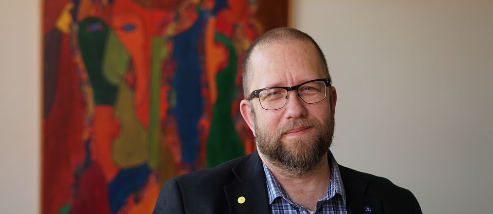 Person i kavaj står framför en färgstark abstrakt målning på väggen.