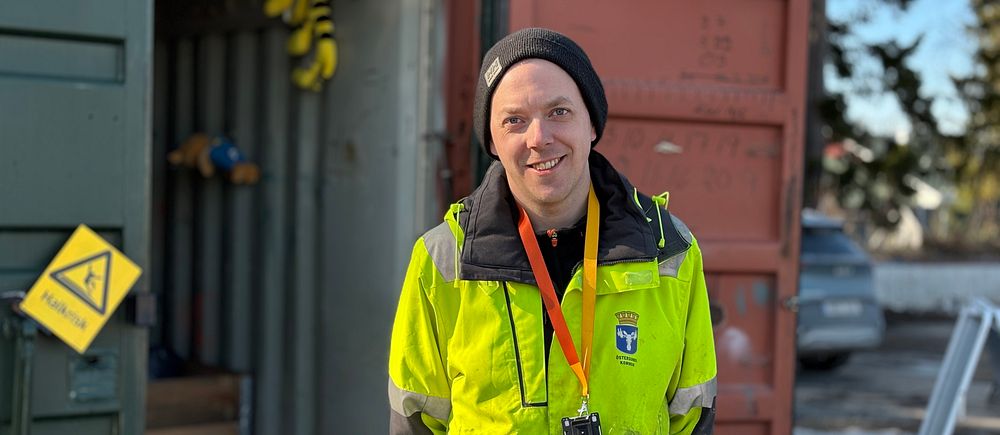 Robin Pettersson på återvinningscentralen i Östersund står med en gul arbetsjacka och står framför den container där man samlar in textilavfall.