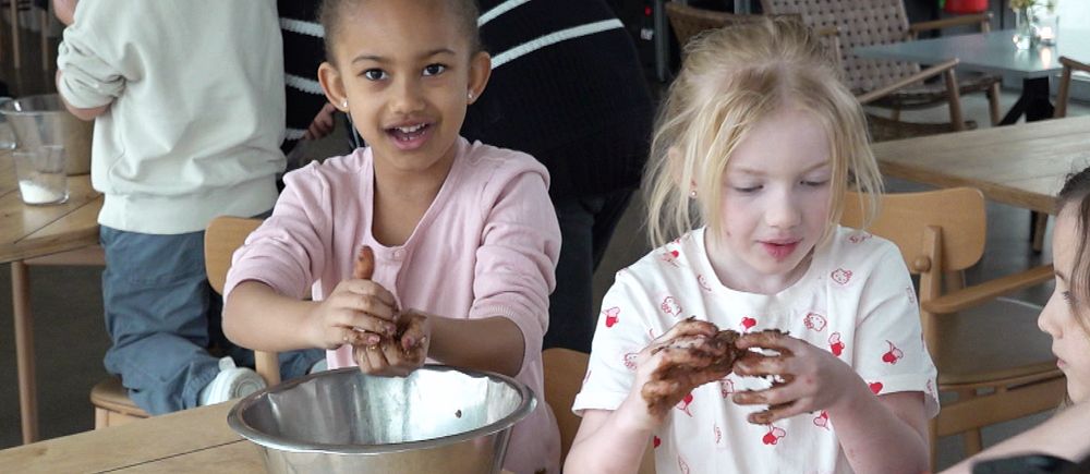 Två flickor i rosa tröjor och uppsatt hår rullar chokladbollar i Pumphuset i Landskrona. Det är en ljus lokal och flera barn syns i bakgrunden.