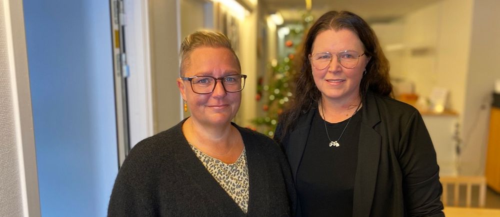 Två kvinnor i svarta kläder står i ett rum.