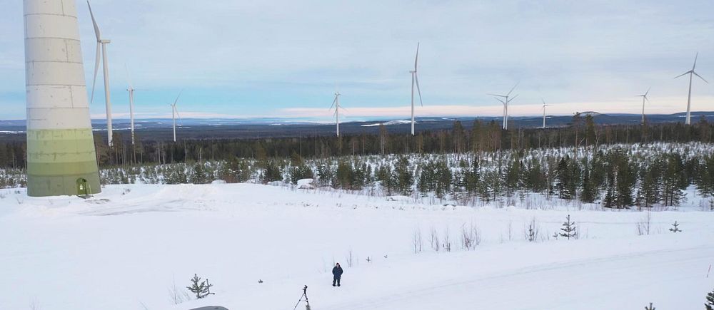 SVT:s reporter fotad av drönare från luften och omgiven av vindsnurror i den gigantiska vindkraftparken utanför Piteå.