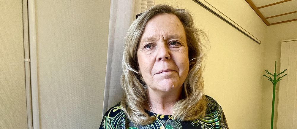 Kvinna i mönstrad klänning i kontorsmiljö, grön klädhängare i bakgrunden.