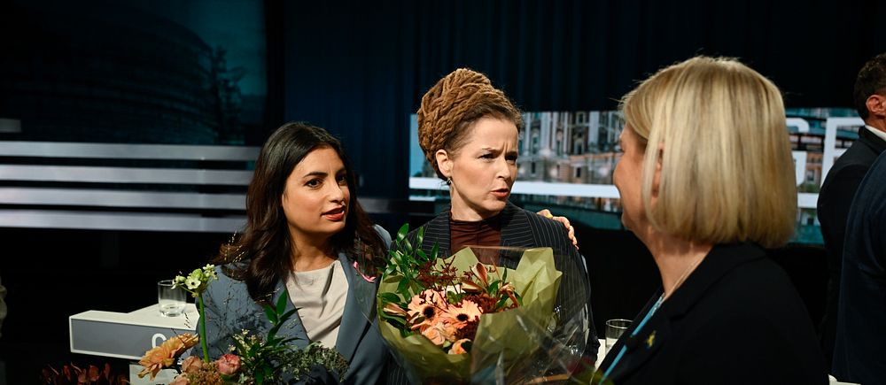 Tre personer står på en scen och håller blombuketter vid ett evenemang eller prisutdelning.