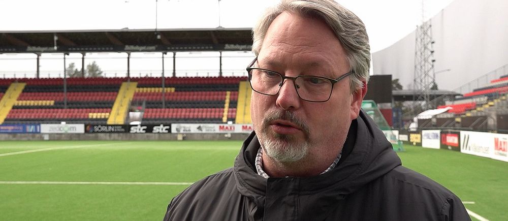 En person står framför en fotbollsplan och läktare på en stadion.