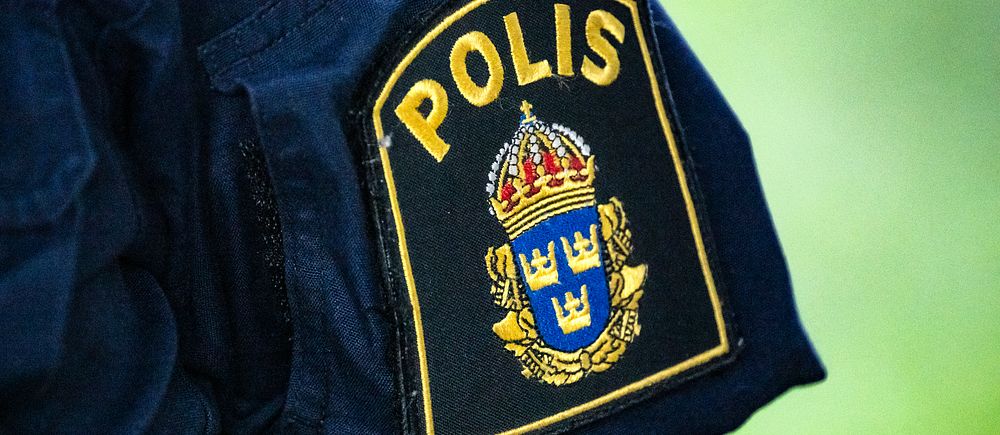 Närbild på svensk polisuniform med polisens emblem på ärmen.