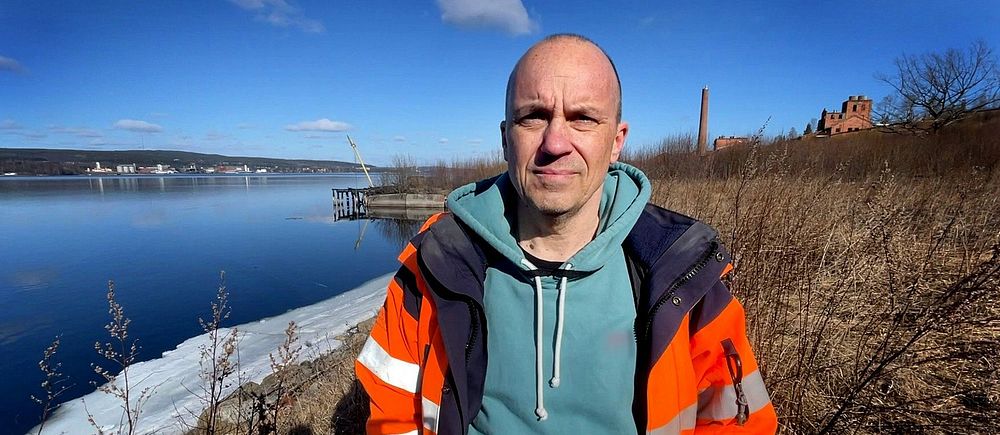 Sven-Åke Westman står på ett gammalt industriområde i Essvik utanför Sundsvall. Han är iklädd varseljacka och tittar in i kameran.