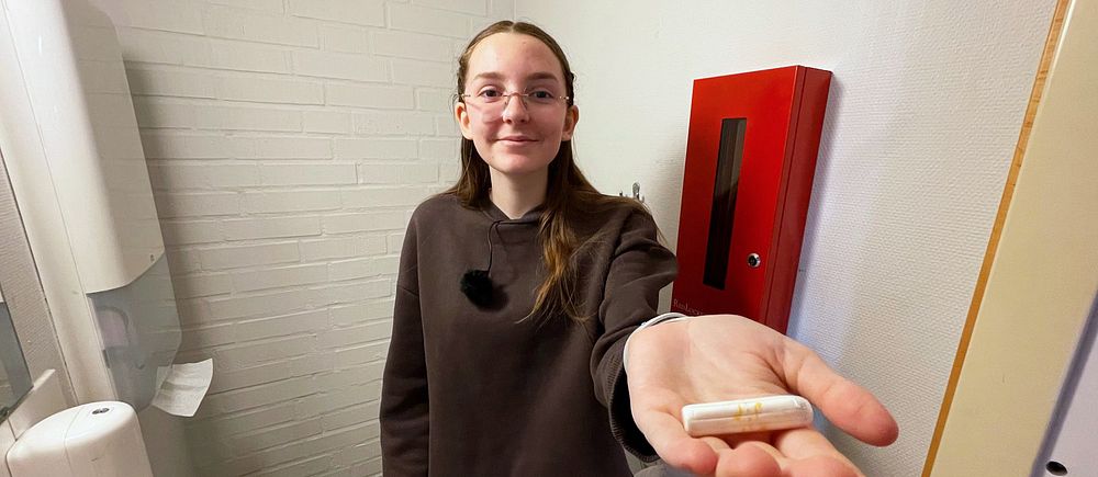 Kvinna håller ut en mindre föremål i sin hand, står i ett badrum.