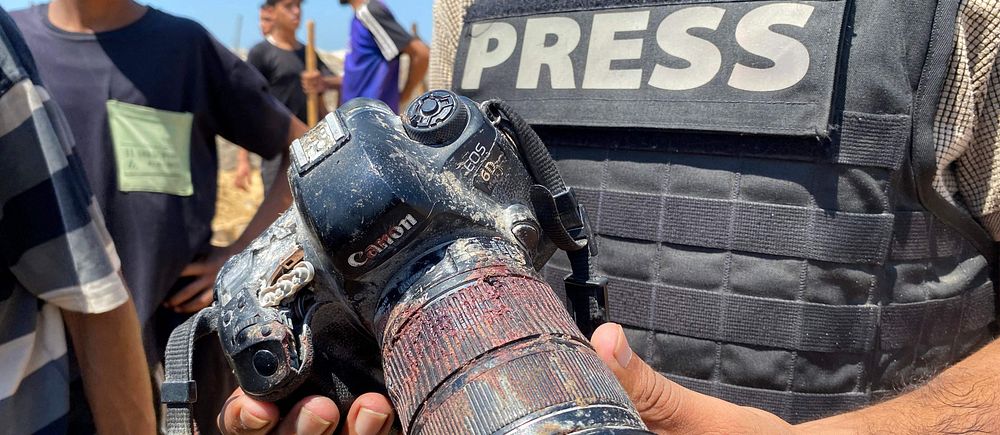Journalist visar upp en skadad kamera med brända och smutsiga delar.