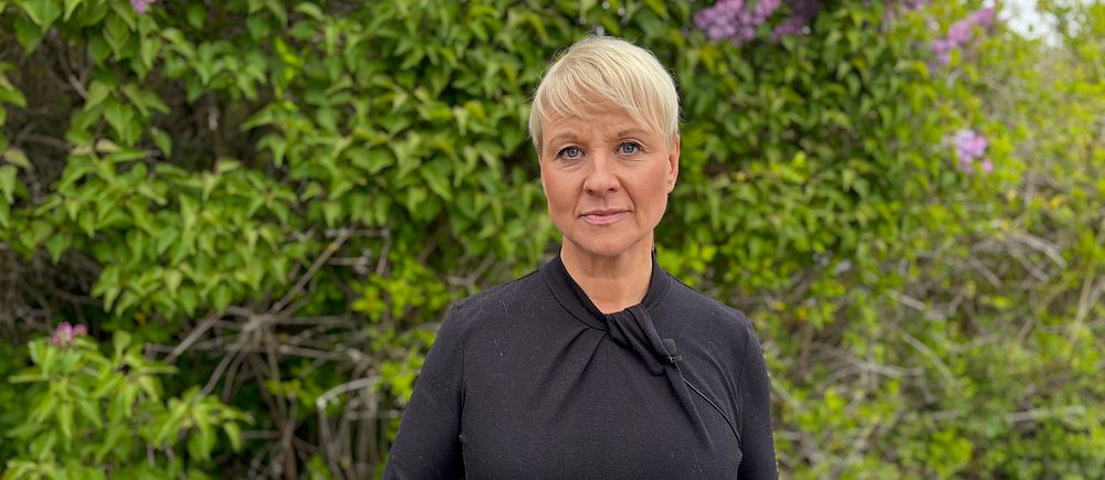 Äldre- och socialförsäkringsminister Anna Tenje (M) står framför blommande buskar utomhus.