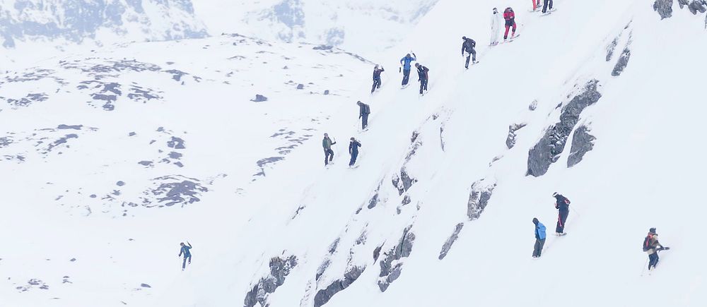 Flera personer klättrar uppför en brant och snötäckt bergssida i vinterlandskap.