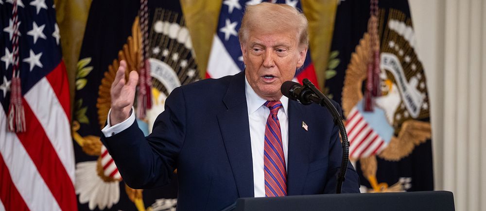 Person vid presidenttalspodium med amerikanska flaggor och presidentens sigill i bakgrunden.