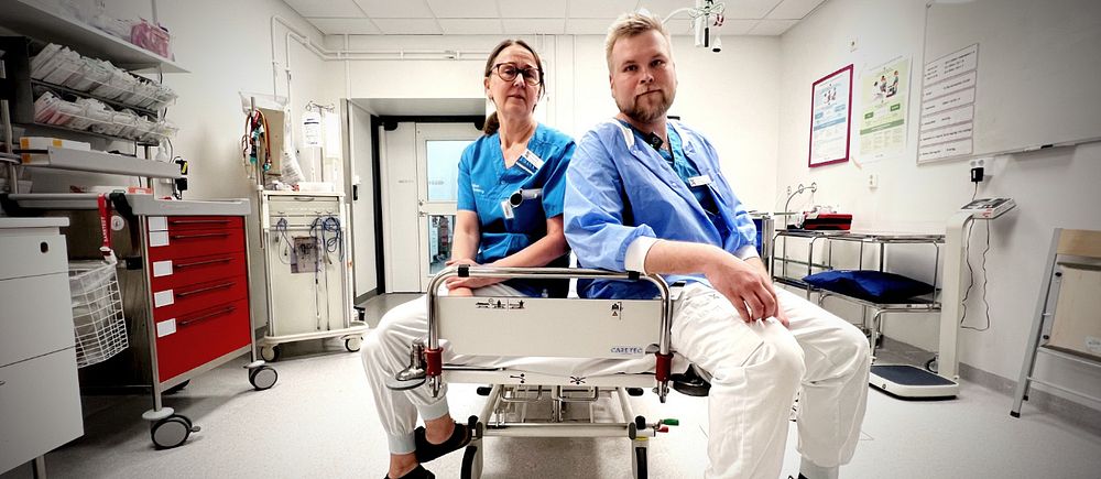 Två sjukvårdsanställda sitter på en brits i ett sjukhusrum.