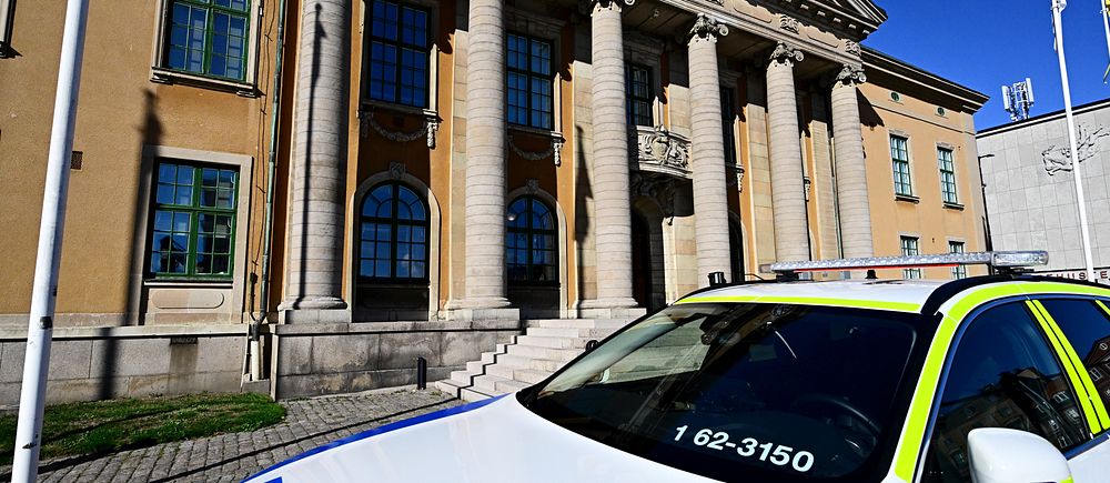 Polisbil parkerad framför byggnad med pelare och stor ingång, Blekinge tingsrätt på Karlskronas stortorg, med klarblå himmel i bakgrunden.