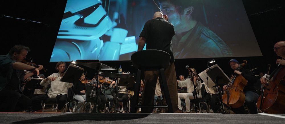 En dirigent leder orkester framför en stor filmskärm som visar en filmscen ur Star wars.