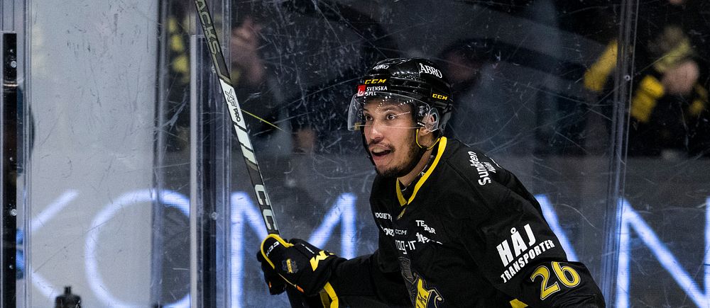 Ishockeyspelaren i svart uniform med nummer 26 håller klubban på isen.