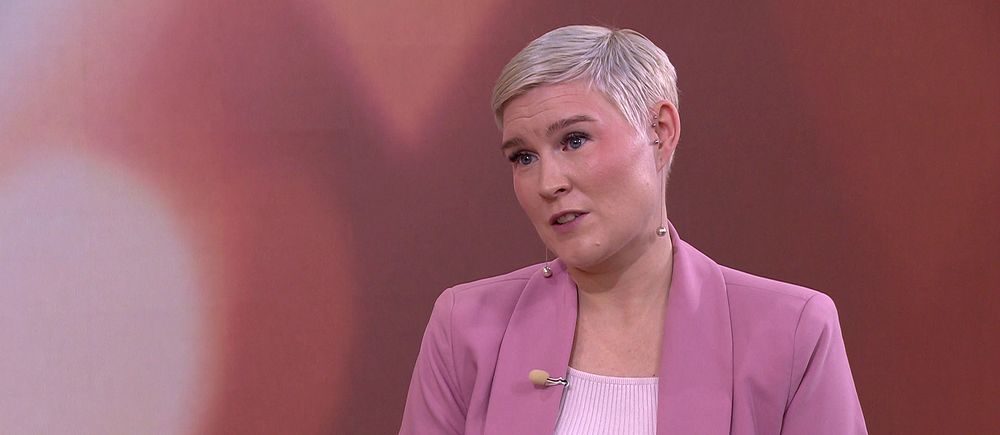 Milly Carlsson i rosa kavaj framför brun bakgrund.