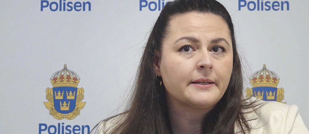Kvinna sitter framför en vägg med svenska polisens logga.