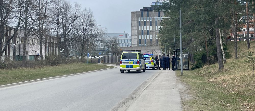 Polisbil och poliser vid en gata i ett bebyggt område.