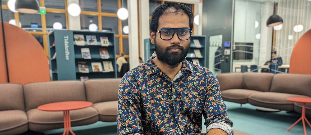 Studenten Ebin Ephrem Elavathingal sitter i en brun soffa i Mälardalens universitets bibliotek i Eskilstuna