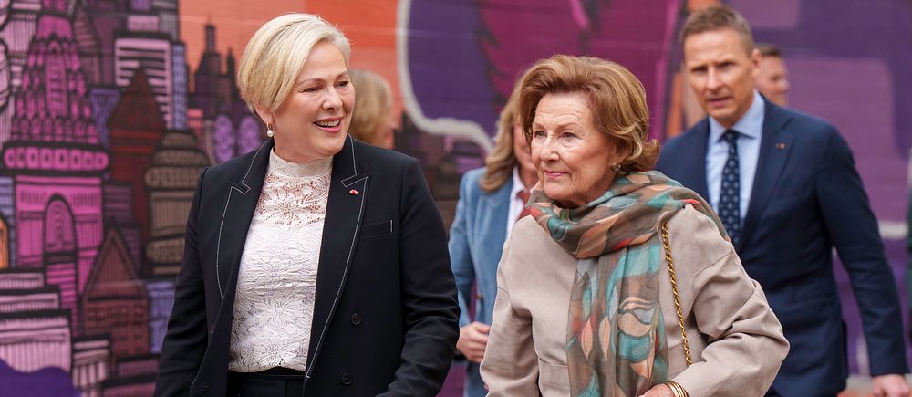 Personer promenerar framför en färgglad väggmålning. En annan man följer efter.