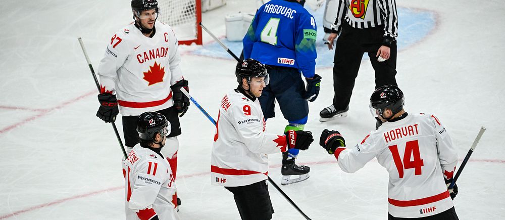 Fyra kanadensiska ishockeyspelare firar på isen under match mot blåklädda motståndare.