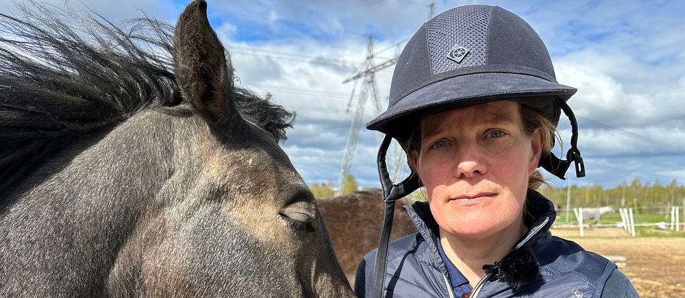 En person med ridhjälm står nära en häst som nosar mot personens axel utomhus.