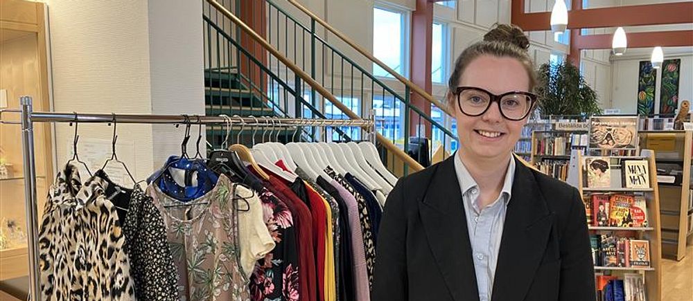En person står vid ett klädställ med färgglada plagg i en butiksmiljö.