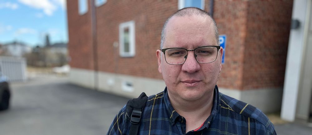 Åklagare Jonas Fjellström – en medelålders man i flanellskjorta och glasögon framför en tegelbyggnad