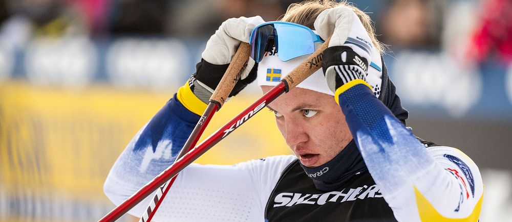 Skidåkare i tävlingsdräkt med nummer 4 dricker ur blå flaska.