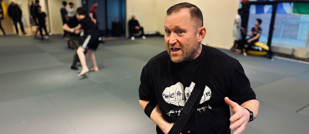 Personer tränar kampsport i en dojo med grå mattor och flaggor på väggarna. I förgrunden Jörgen Hamberg, ordförande för Västerås fight club.