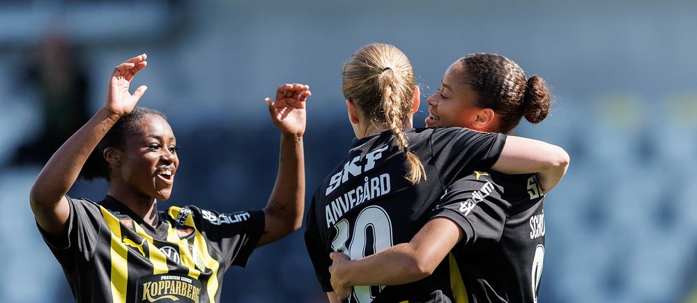 Tre fotbollsspelare i svartgula matchställ firar tillsammans på planen.