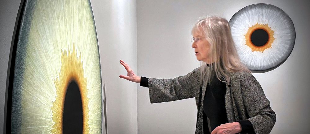 Kvinna gestikulerar framför stor konstinstallation med ögonmotiv på vägg.
