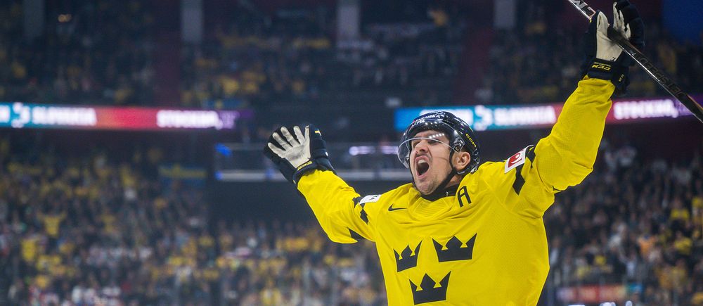 En svensk ishockeyspelare firar mål med armarna i luften inför jublande publik.