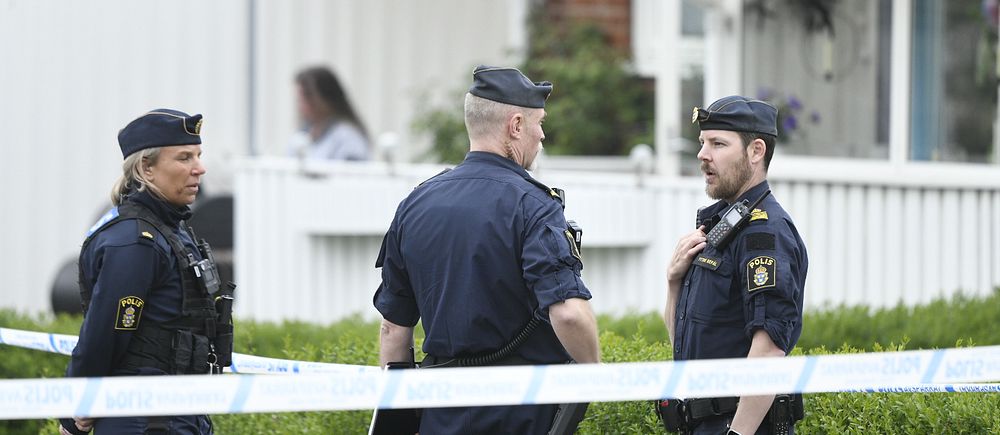 Tre poliser samtalar vid avspärrning utanför ett bostadshus i Klippan, kvinna syns i bakgrunden.