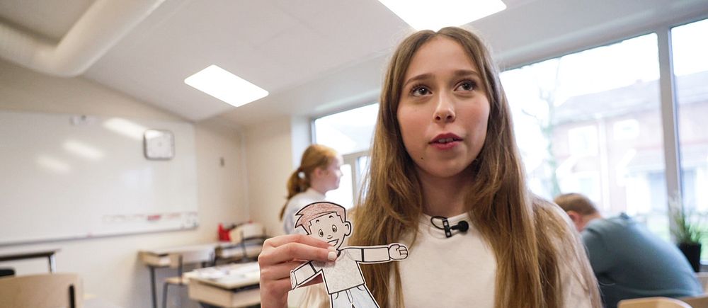 En tjej står i ett klassrum och håller i en tecknad gubbe