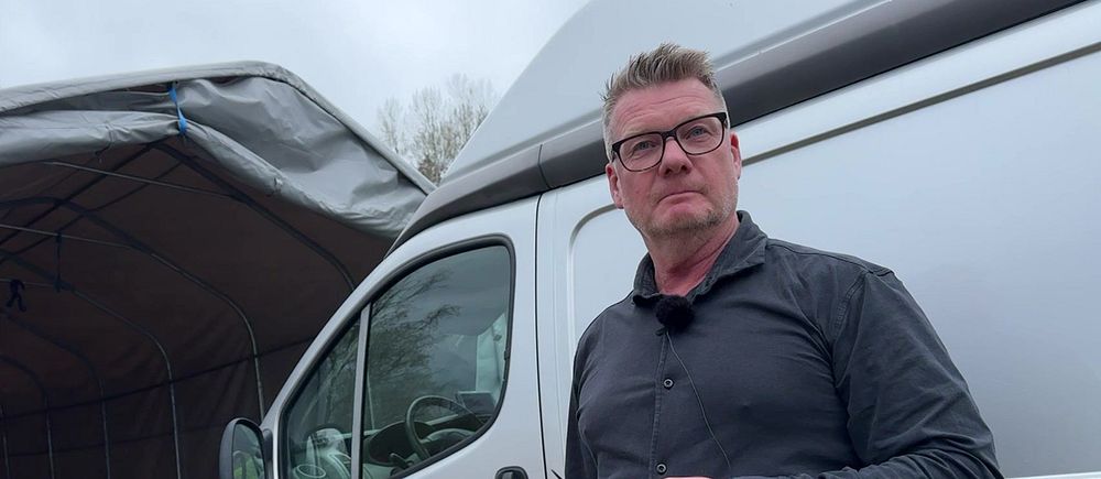 En person står framför en silverfärgad skåpbil utomhus.