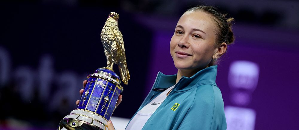 Person i blå tröja håller upp en guldprydd pokal med en fågel på toppen.