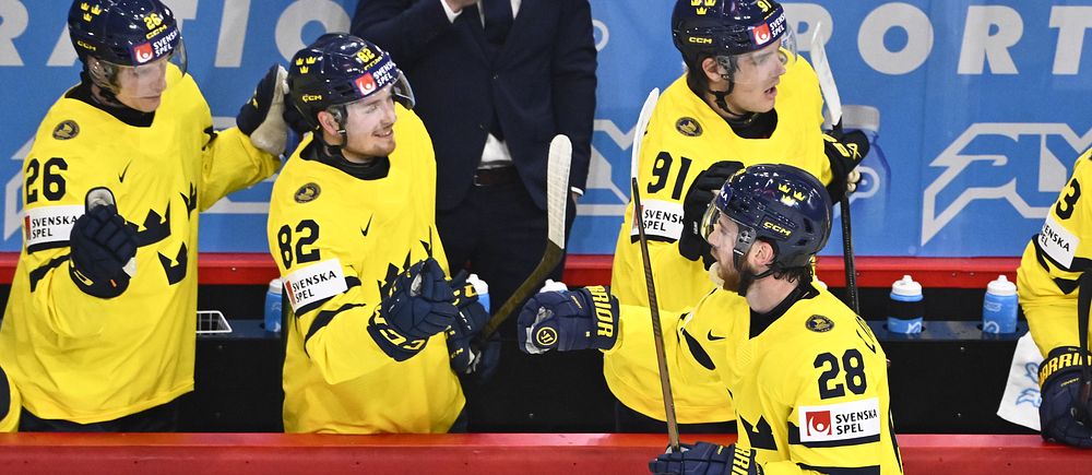 Ishockeyspelare i Tre Kronors gula tröjor firar vid båset under match.