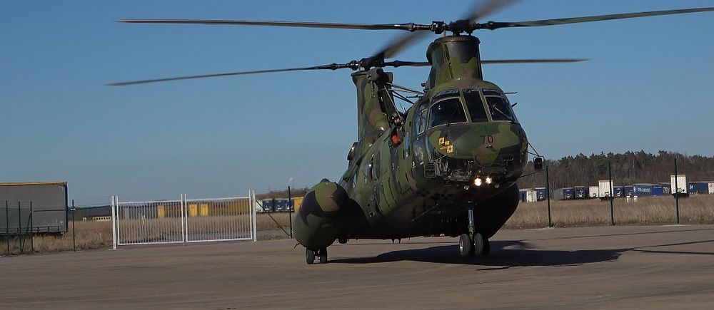 Militärhelikopter står på en flygplats, en klar blå himmel i bakgrunden.