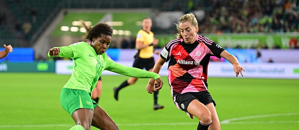Två damfotbollsspelare i kamp om bollen under en match på en gräsplan.