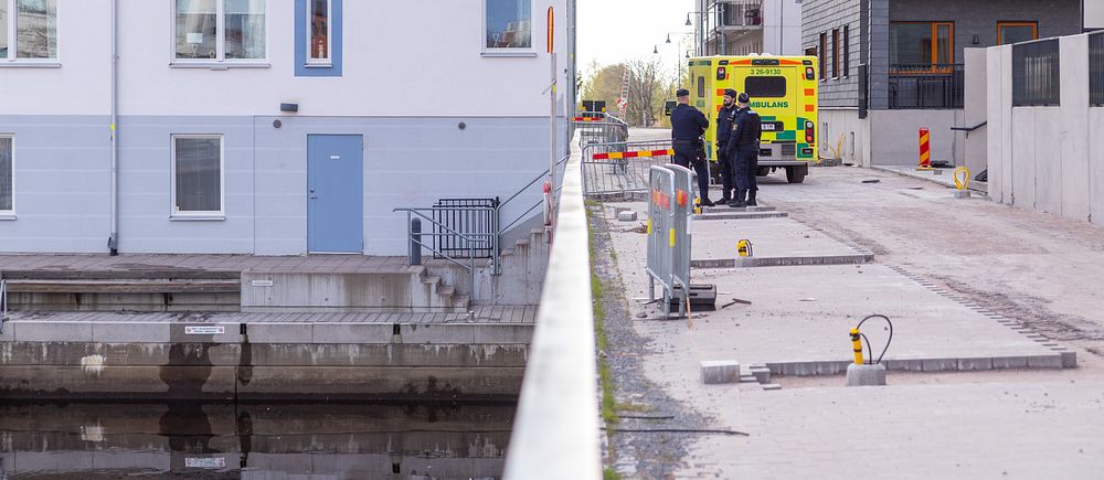 Ambulans och polis på gata vid bostadshus nära vattnet.