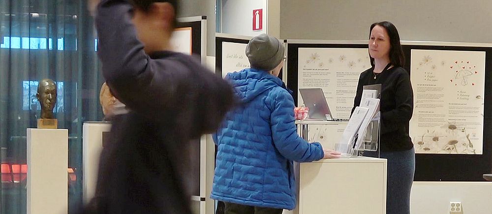 En person går förbi kameran medan en annan ställer frågor till Kristina Kleemo som står vid Luleå kommuns monter på Kulturens hus.
