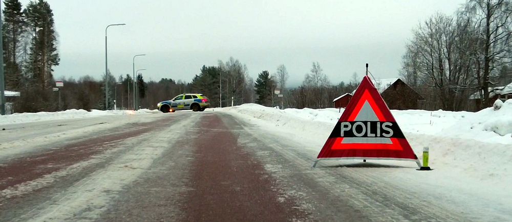 En väg med en uppställd triangel som det står ”polis” på . i bakgrunden syns en polisbil