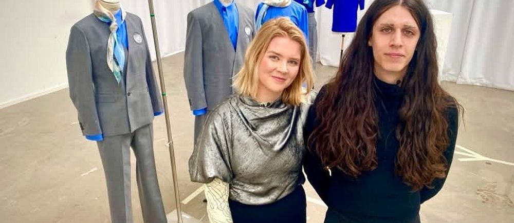 Två personer står framför skyltdockor med blå arbetskläder och kostymer i ett showroom.