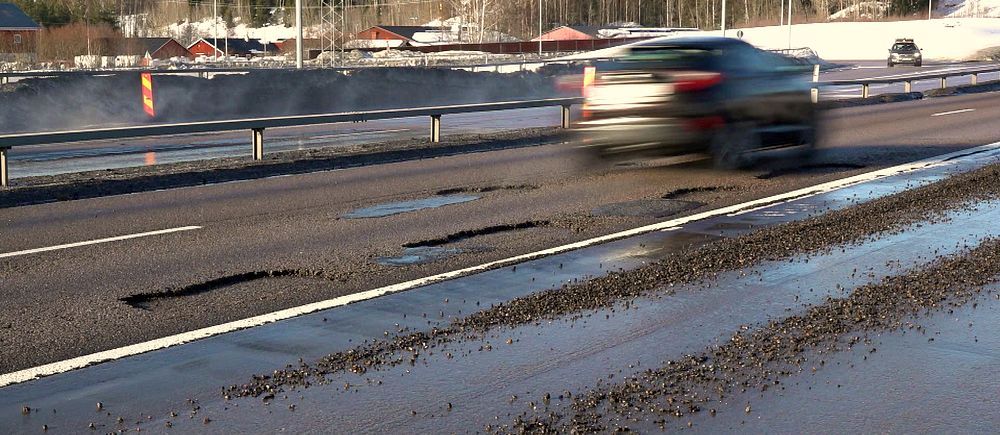 En bil passerar gropar och skador på en motorväg under vintersäsong.