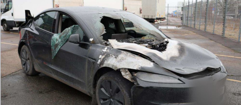 Kraftigt krockskadad svart personbil med bucklig motorhuv och krossat främre fönster.