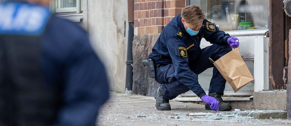 Polis samlar bevis vid trasigt glas på trottoaren. En annan polis vänd mot kameran.