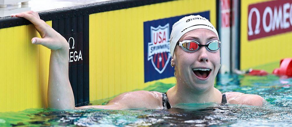 Simmare tar i kanten vid mål efter lopp i simbassäng, USA Swimming-skylt syns i bakgrunden.